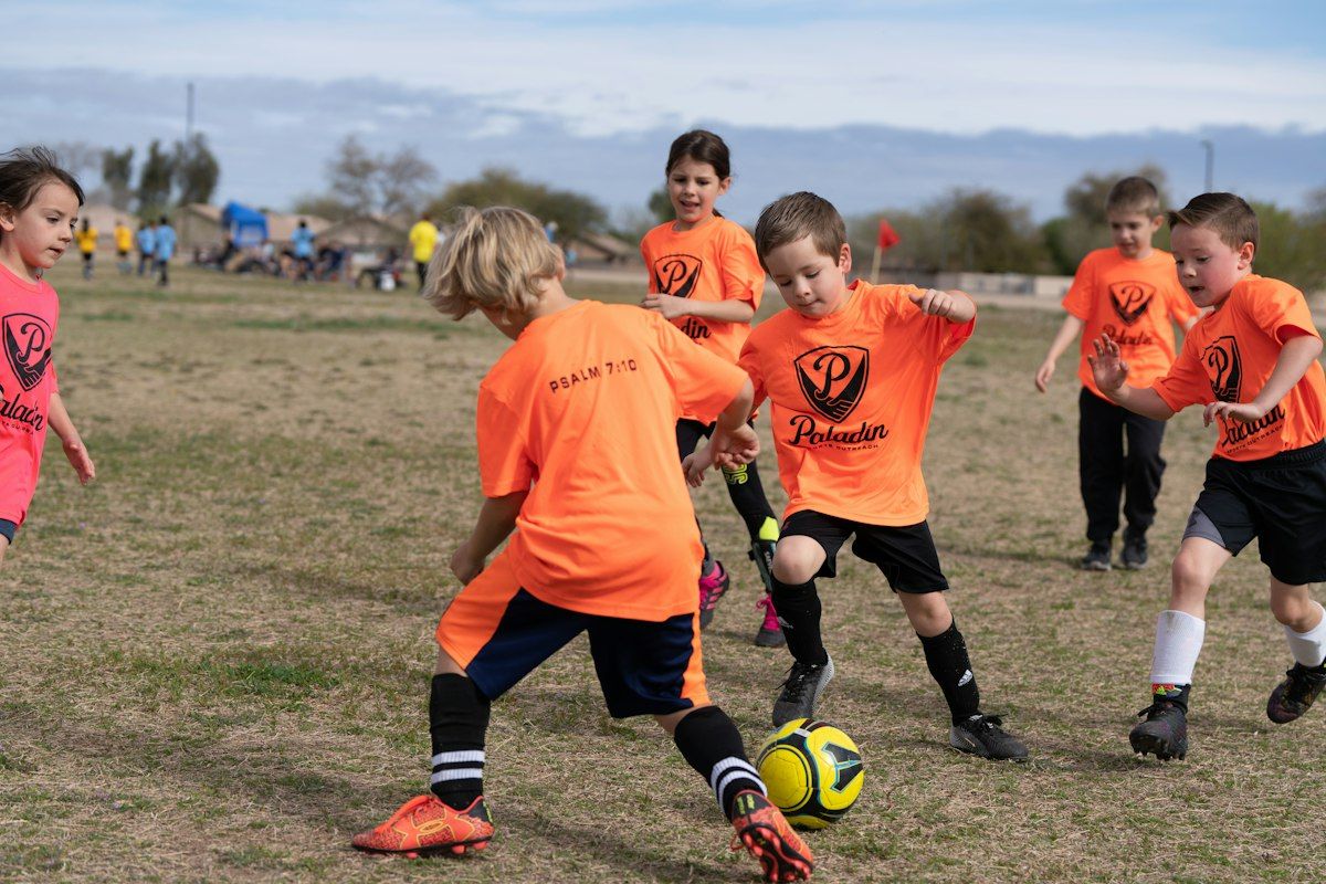 Young children in orange jerseys playing soccer outdoors