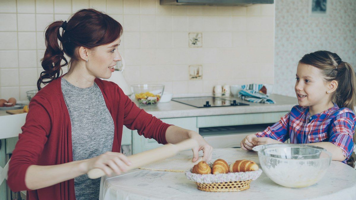 Mom and daughter rolling dough together in a sunny kitchen