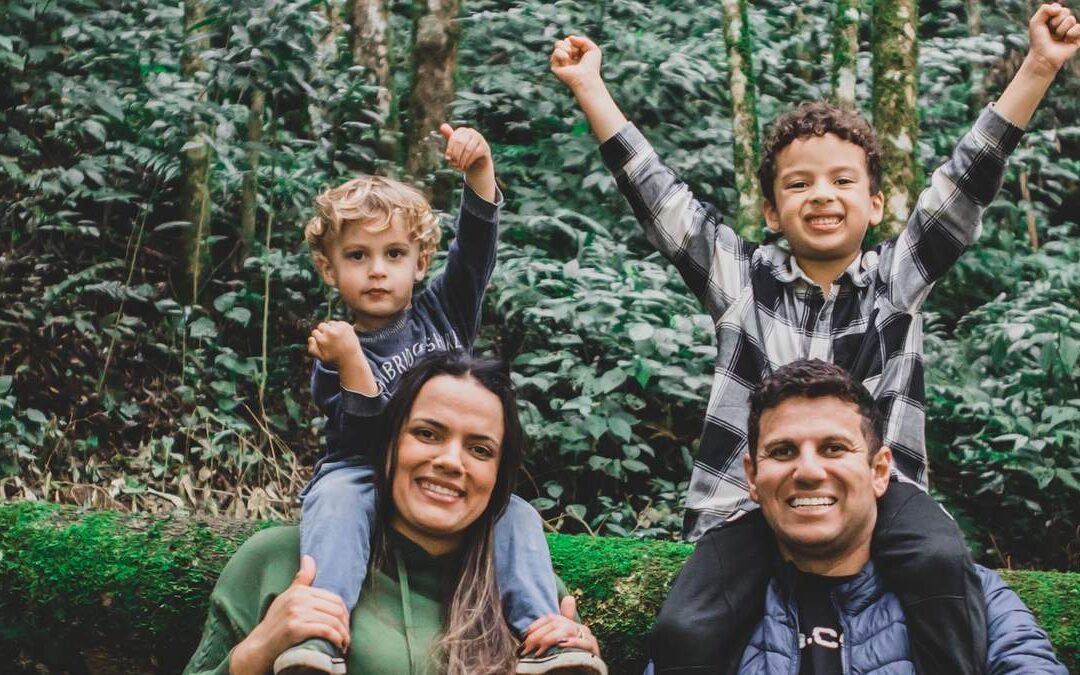Smiling parents carrying their two cheering sons on their shoulders on a green forest trail
